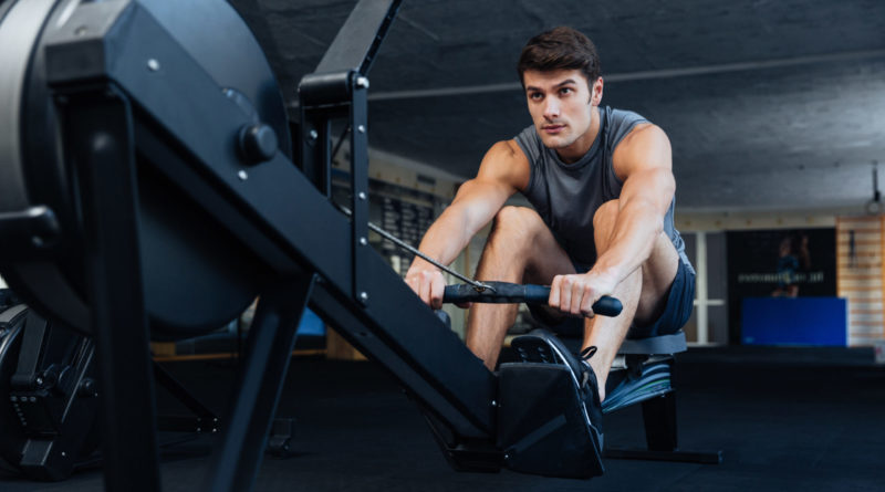 Fitness young man using rowing machine in the gym